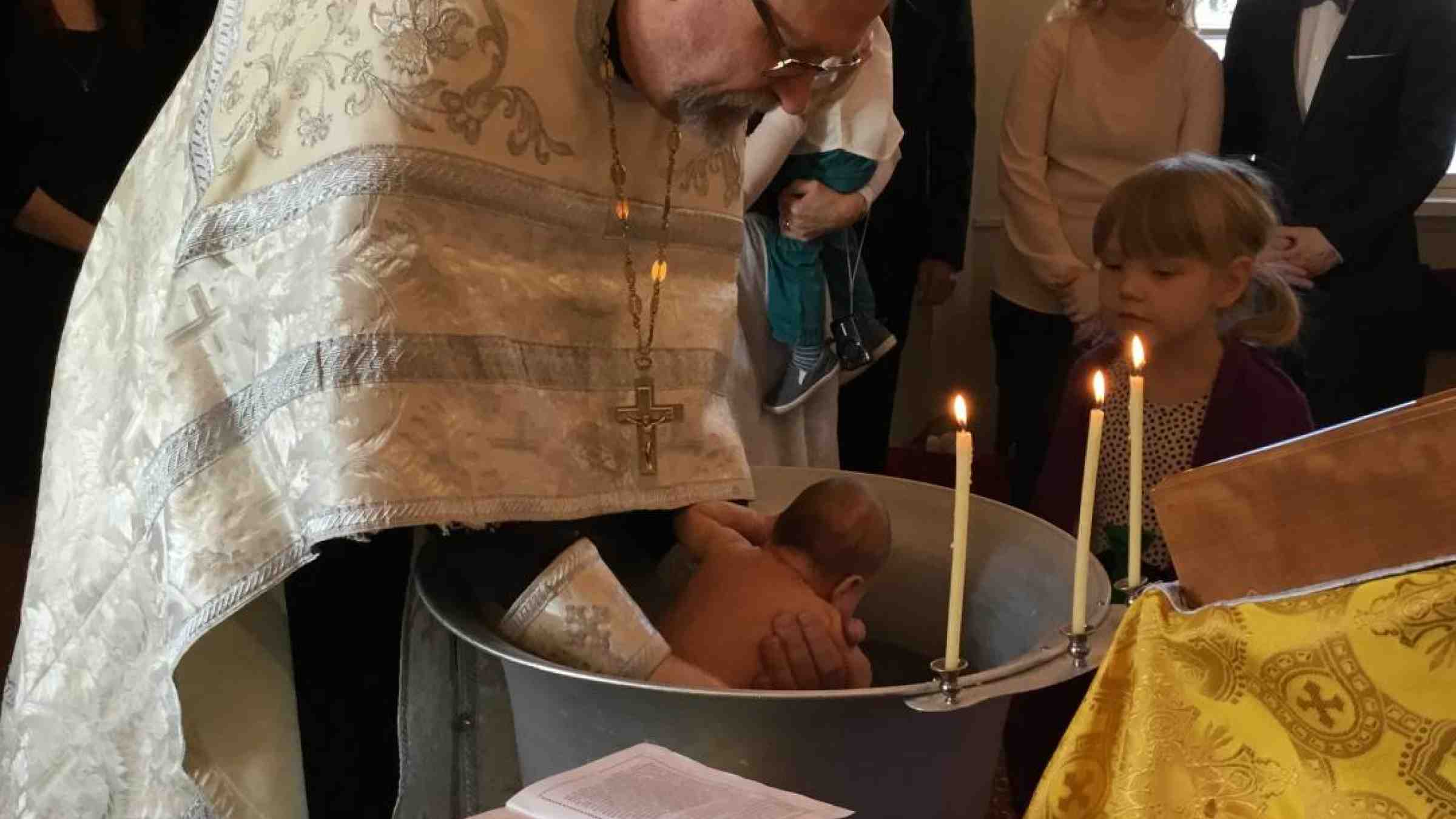 Ortodoksipappi kastaa lapsen upotuskasteella