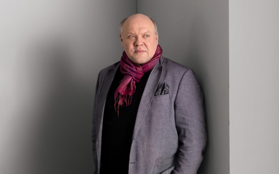 Näyttelijä Hannu-Pekka Björkman seisoo harmaan seinän edessä