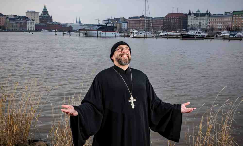ortodoksipappi isä Johannes Lahtela seisoo meren rannalla Helsingissä kädet levitettyinä ja katse kohti taivasta