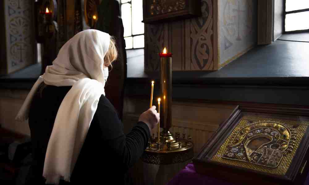 Valkoisella huivilla päänsä peittänyt ortodoksinainen sytyttää tuohuksen Jumalanäidin ikonin edessä