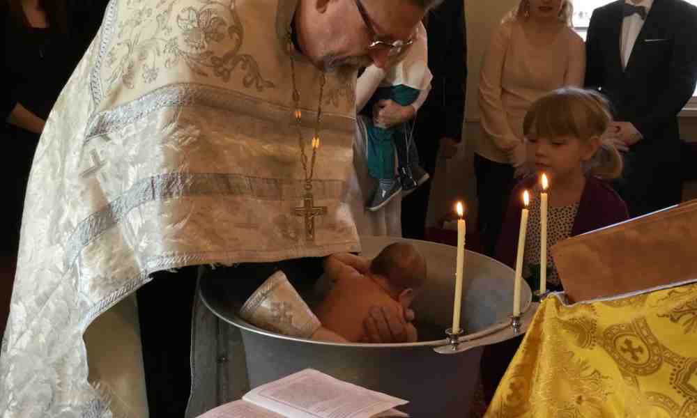 Ortodoksipappi kastaa lapsen upotuskasteella
