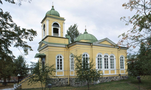 Savonlinnan keltainen ja vihreäkattoinen Pikkukirkko kuvattuna kesäaikaan pilvisenä päivänä