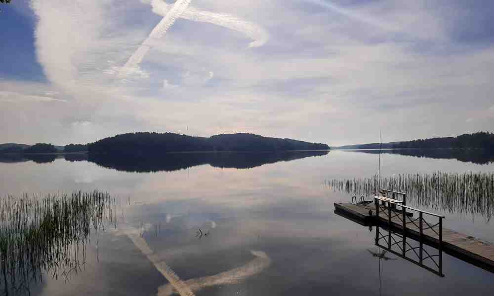 Suihkukoneiden juovat muodostavat taivaalle ristin, joka heijastuu järven pintaan